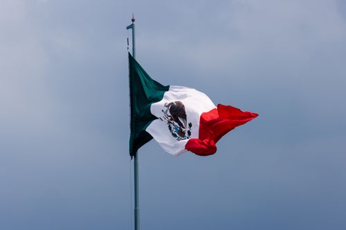 Free Vibrant Mexican flag waving prominently against a dramatic cloudy skyline in Ciudad de México. Stock Photo
