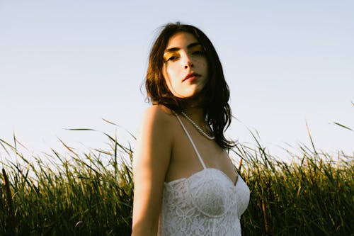 Young Woman in a White Top Standing on a Field in Sunlight