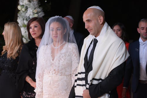 Man in Black and White Striped Suit Standing Beside Woman in White Floral Lace Wedding Dress