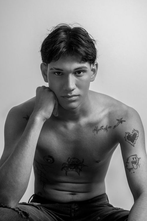 Free Black and white studio portrait of a tattooed man sitting shirtless, exuding confidence and style. Stock Photo