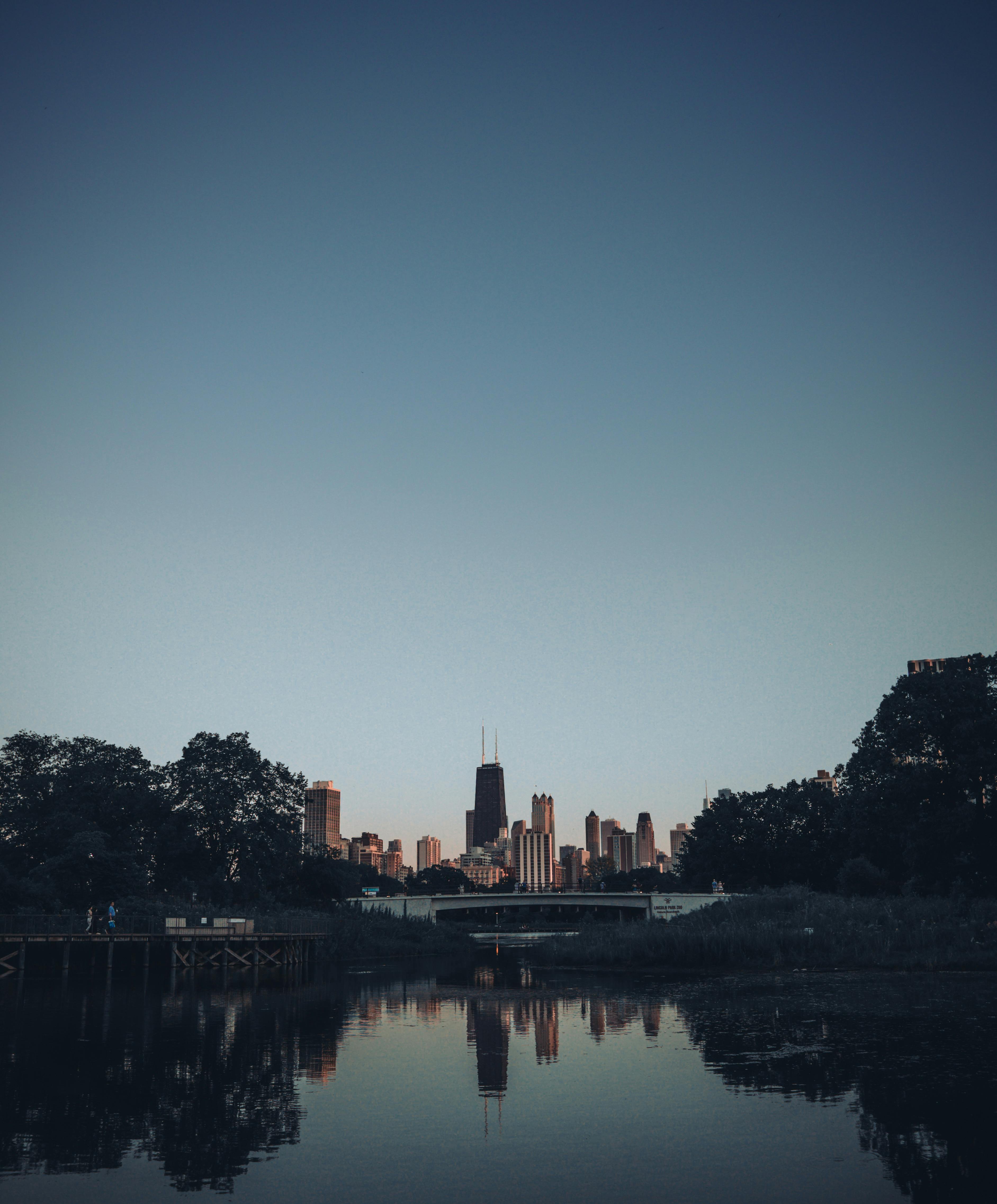City skyline reflecting in calm water at twilight, showcasing urban architecture and natural surroundings.