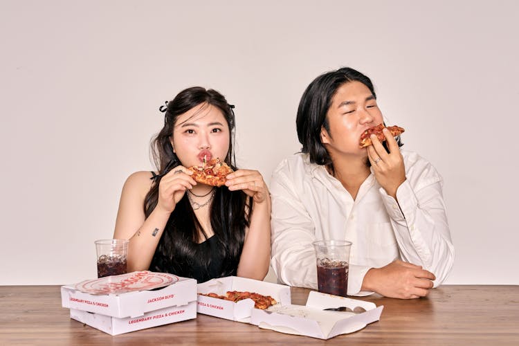 Young Woman And Man Sitting At A Table And Eating Pizza