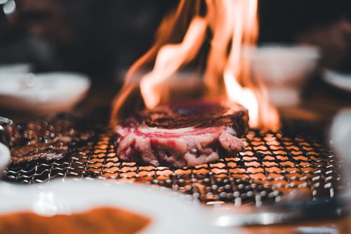 Free Close-up of a steak being grilled on a charcoal BBQ with visible flames, creating an appetizing view. Stock Photo