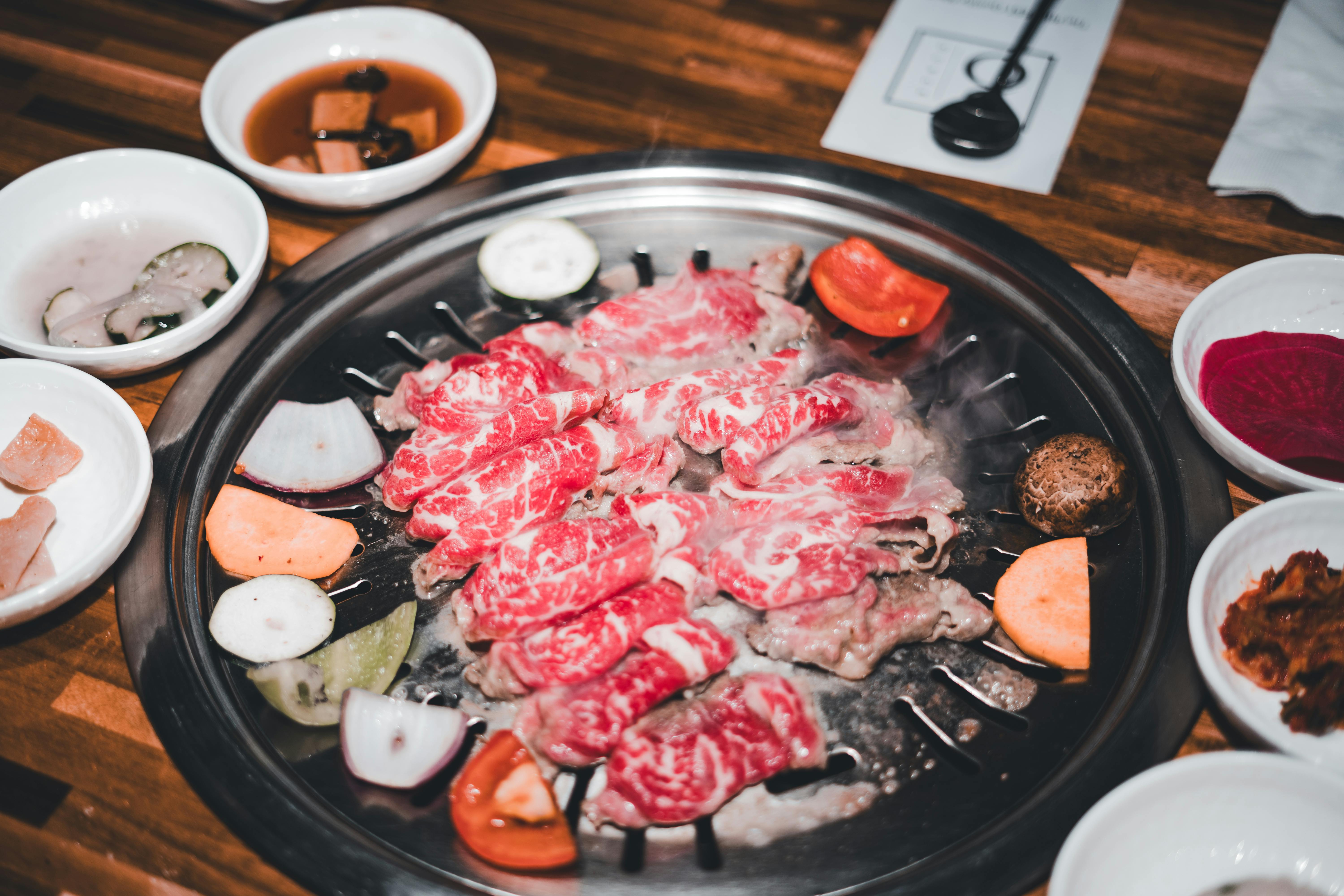 Delicious marbled beef slices grilling on a Korean BBQ with assorted side dishes.