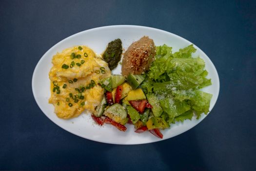 Scrambled eggs, fresh salad, and greens on a white plate for a hearty meal.