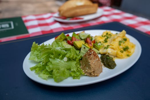 A delicious and nutritious breakfast with vegetables, scrambled eggs, and hummus on a white plate.