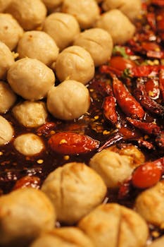 Close-up of spicy Thai meatballs with red chili peppers in a rich sauce, vibrant street food dish.