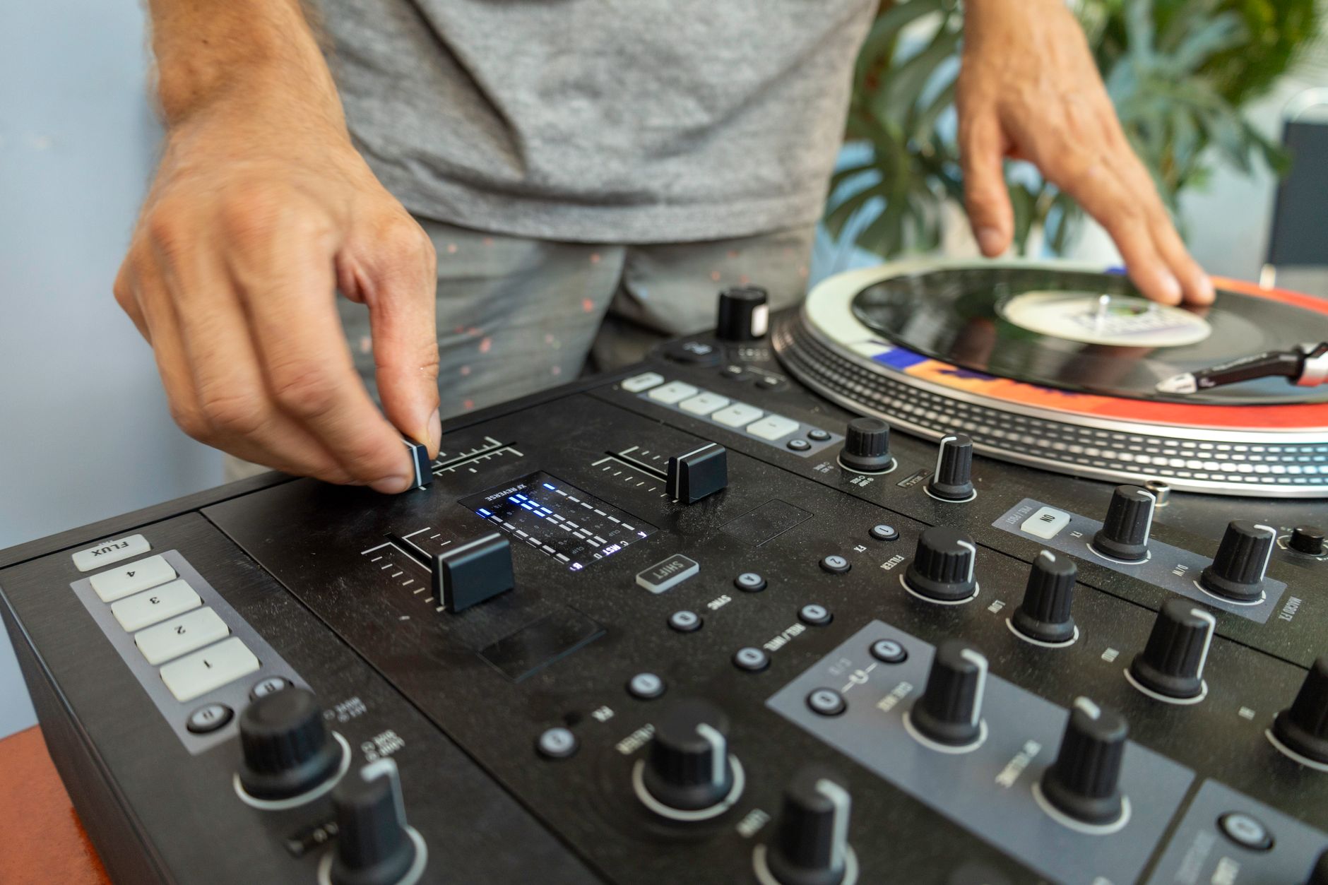 Close-up of a DJ mixing a vinyl record on a professional audio mixer indoors.