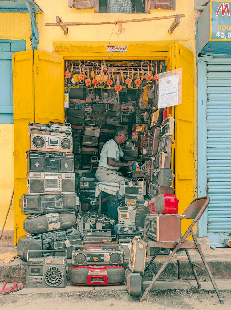 Man Sitting At An Electronics Shop With Stacks Of Old Radios