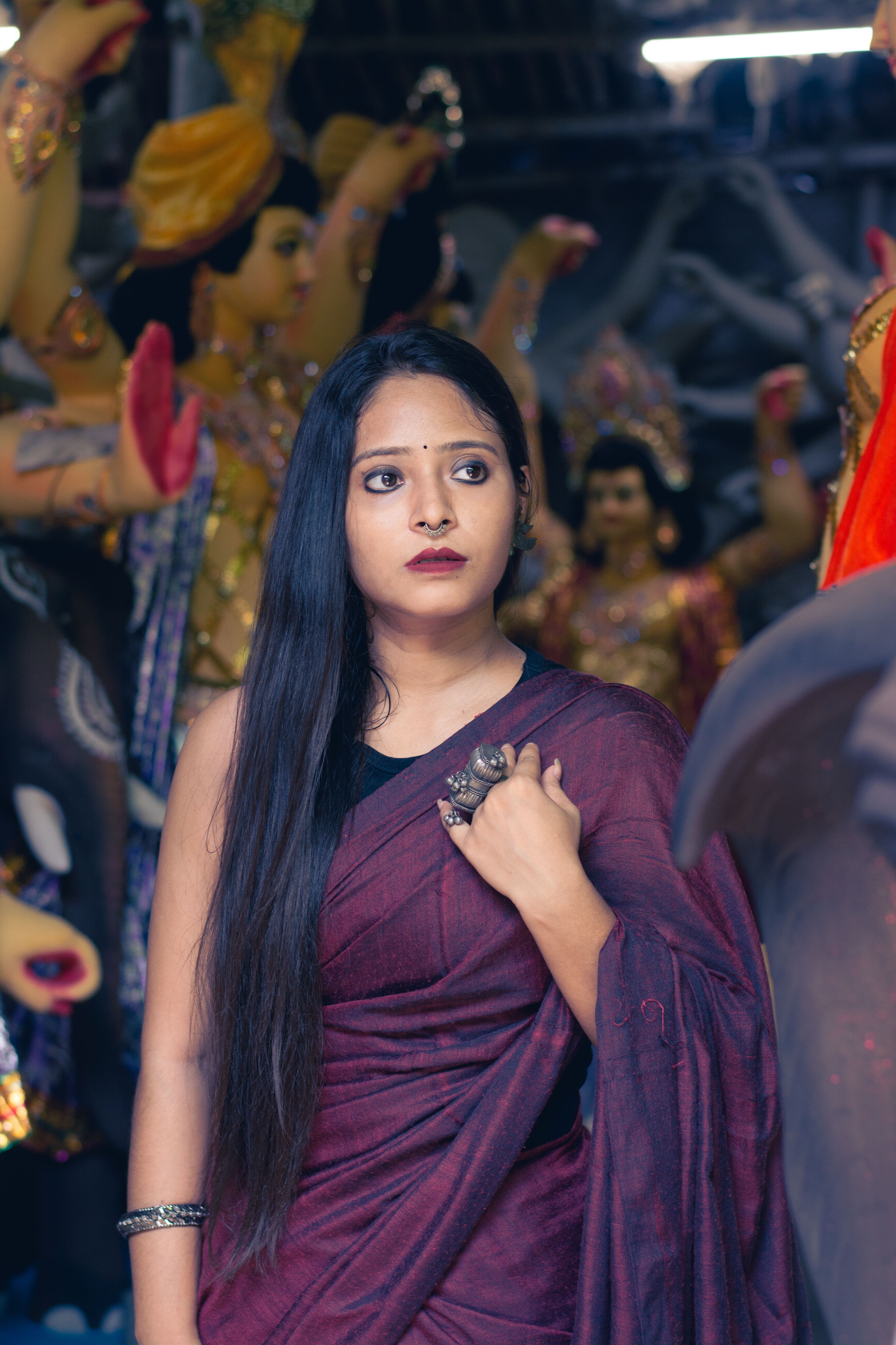 Young woman in traditional saree amidst colorful Hindu idols. Cultural elegance captured in Kolkata.