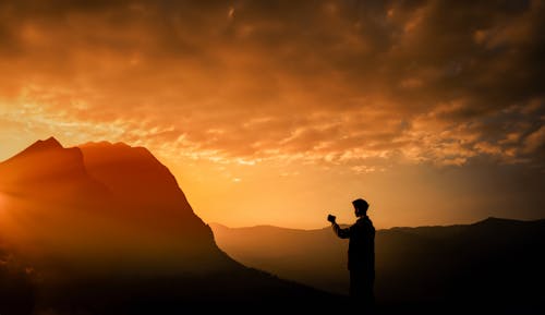 Silhouette of a Man Taking a Photo with his Smartphone of the Sunset Over the Mountains
