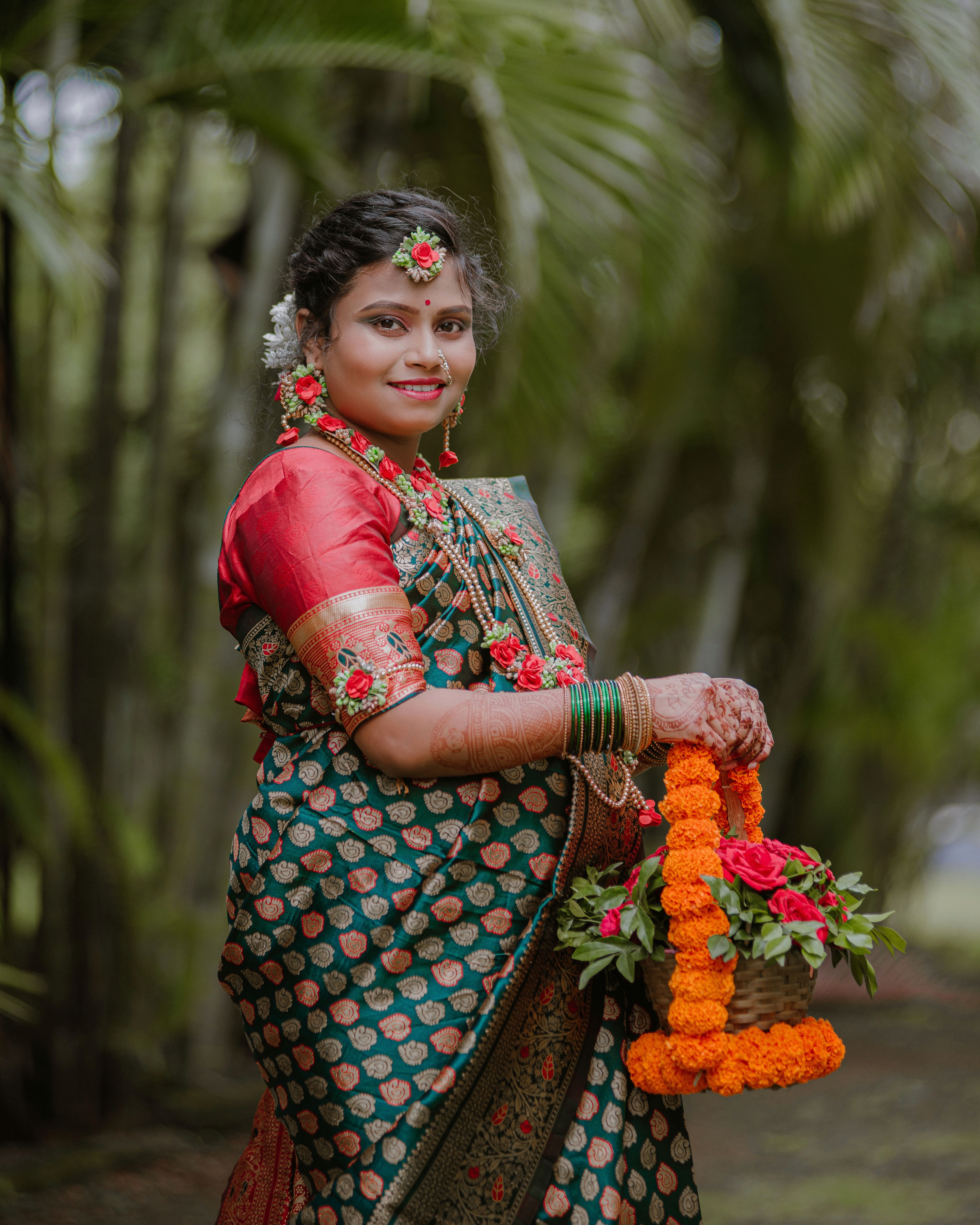 A woman in traditional Maharashtrian attire holds a flower basket outdoors, showcasing cultural beauty.