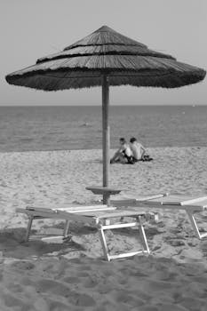 Monochrome image of a beach with umbrella and loungers, capturing a peaceful summer day.