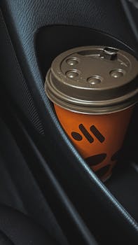 A close-up of a paper coffee cup in a car door holder, showcasing modern automotive interior design.