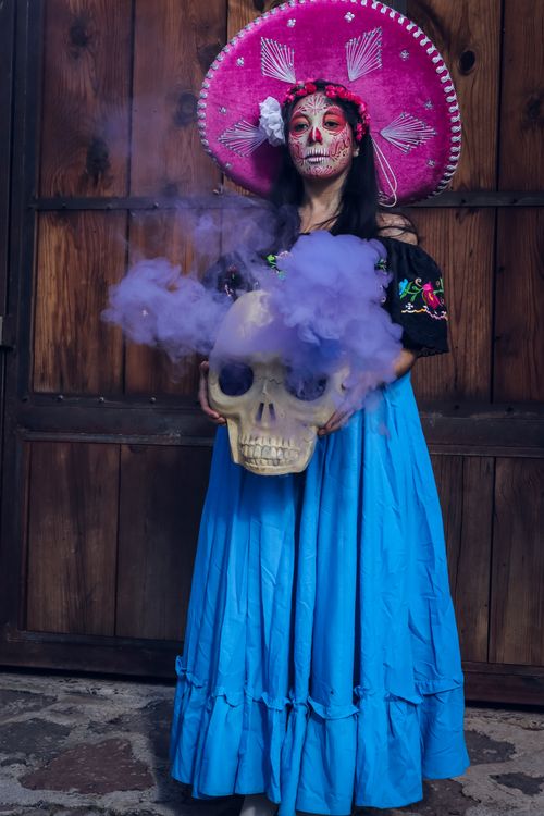 Free A woman in vibrant traditional attire holds a smoking skull for Dia de los Muertos celebration. Stock Photo