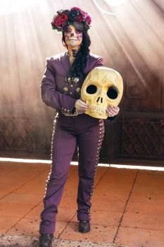 Woman in traditional Day of the Dead attire holding a large painted skull.