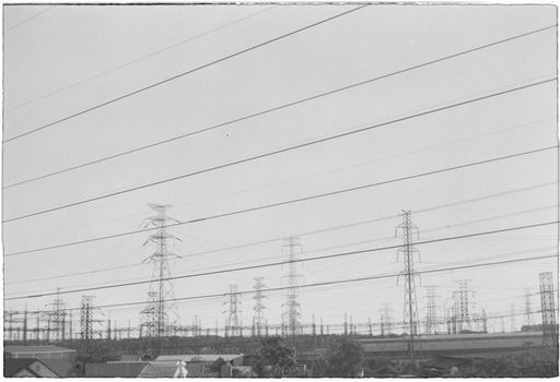 Monochrome image of rows of power lines and pylons in an industrial zone.