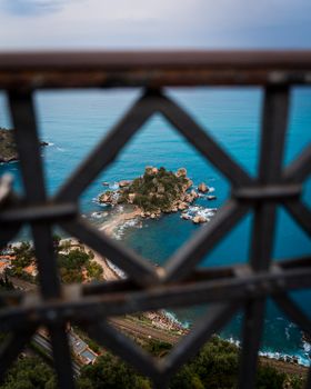 A picturesque coastal view in Sicily through decorative railings, showcasing a small rocky island and clear turquoise waters.