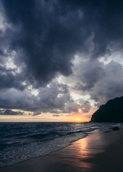 Dramatic beach sunset with dark clouds and reflection over the sea horizon.