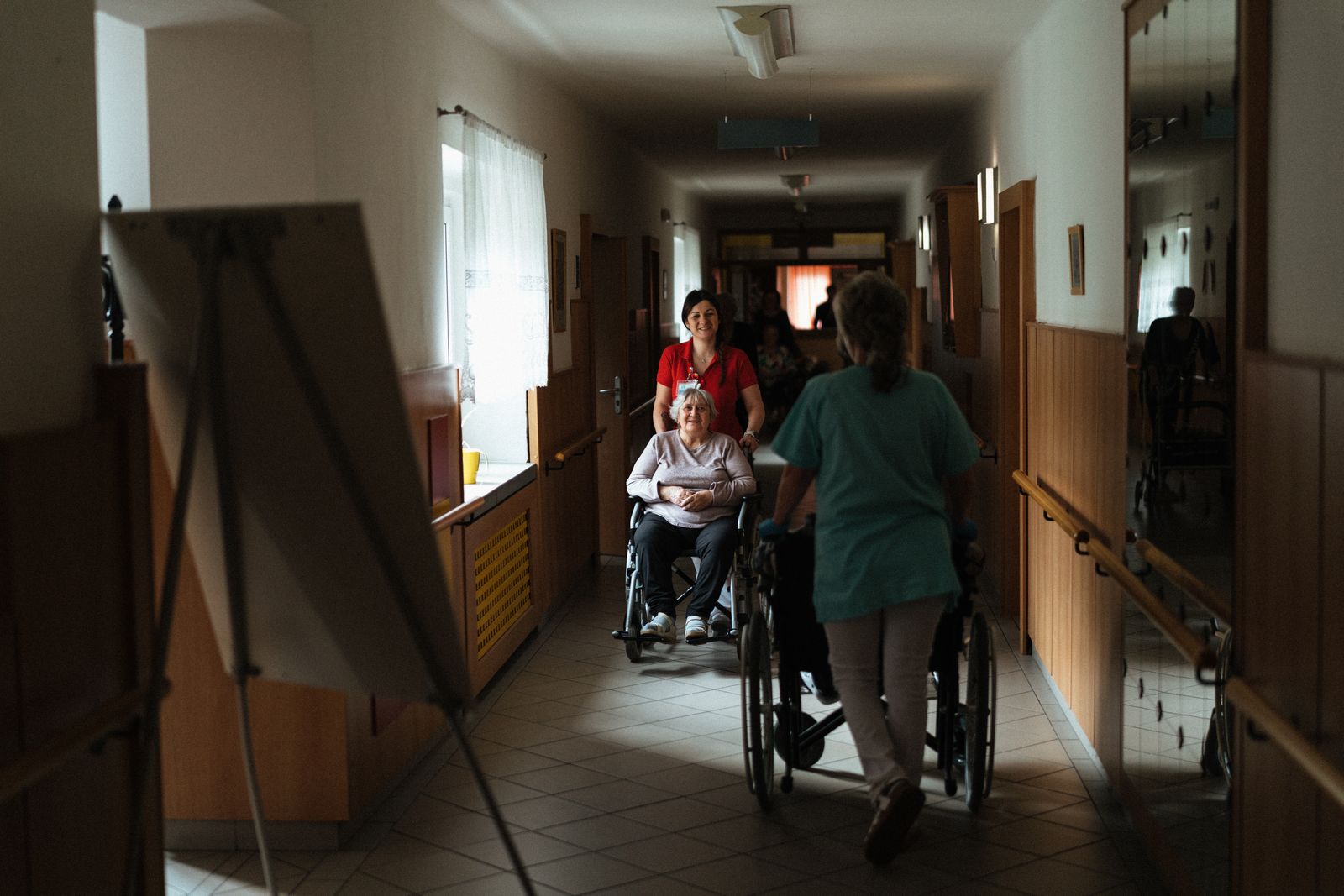 Caregivers assisting seniors with wheelchairs in a long-term care corridor