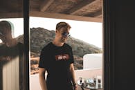 一个时髦男人戴着墨镜，在户外享受休闲时光，身影映在玻璃上