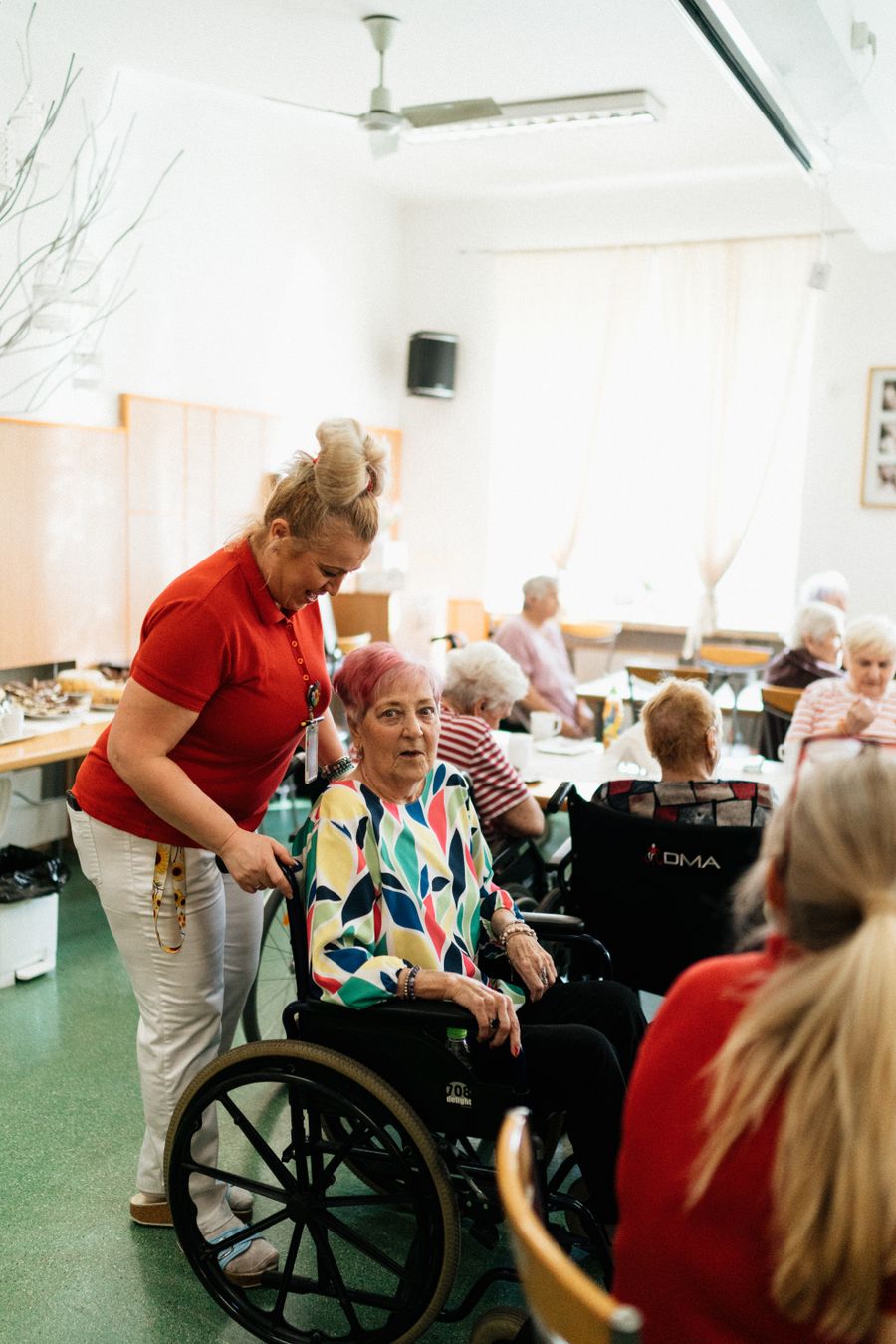 Betreuerin begleitet Seniorin im Rollstuhl zum Termin