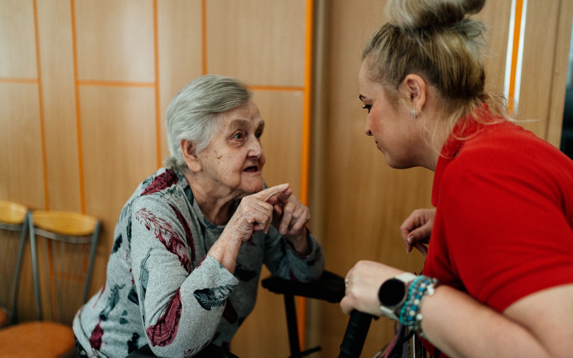 A caregiver and an older woman sitting close together, in a warm and unhurried conversation in a softly lit room.