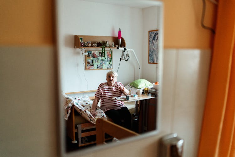 Senior Woman Sitting On A Bed In Retirement Home Room