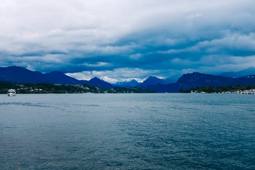A tranquil lake with distant mountains and dramatic overcast skies, capturing nature's beauty.