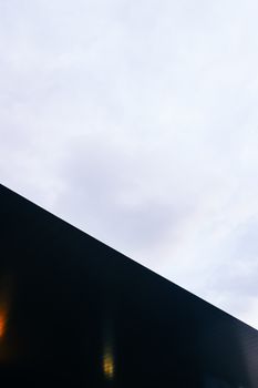 Modern architectural design featuring a diagonal roof silhouette under a cloudy sky.