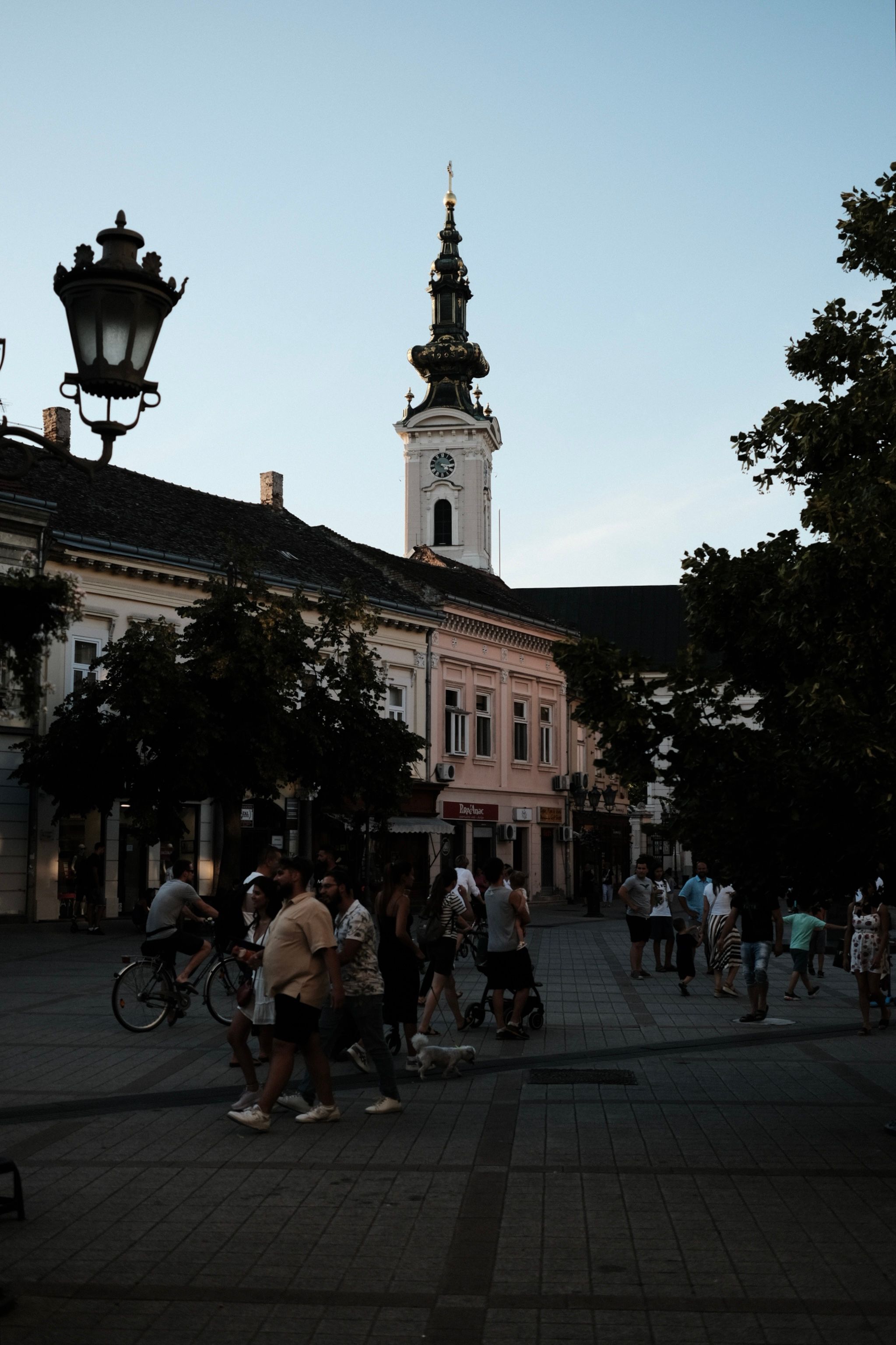 Bustling town square in Novi Sad with Saint George's Cathedral at dusk.