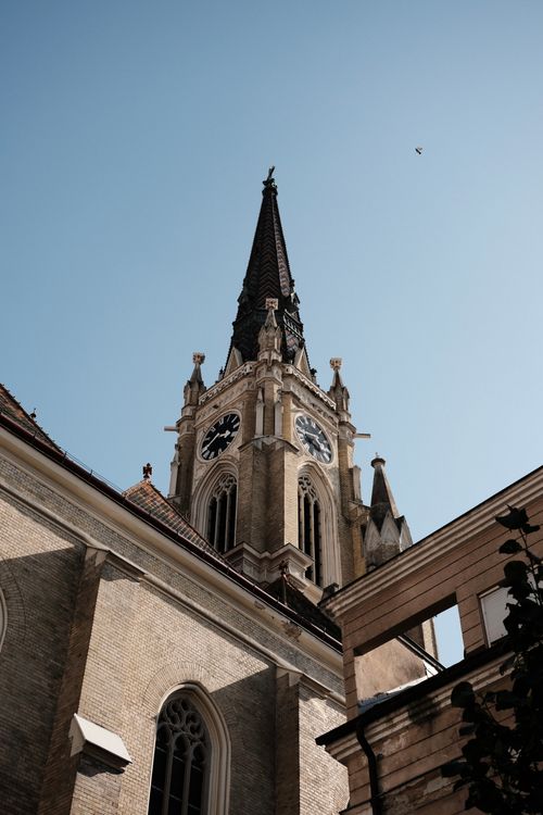 Free A low-angle shot of a Gothic church tower against a clear blue sky in Novi Sad, Serbia. Stock Photo