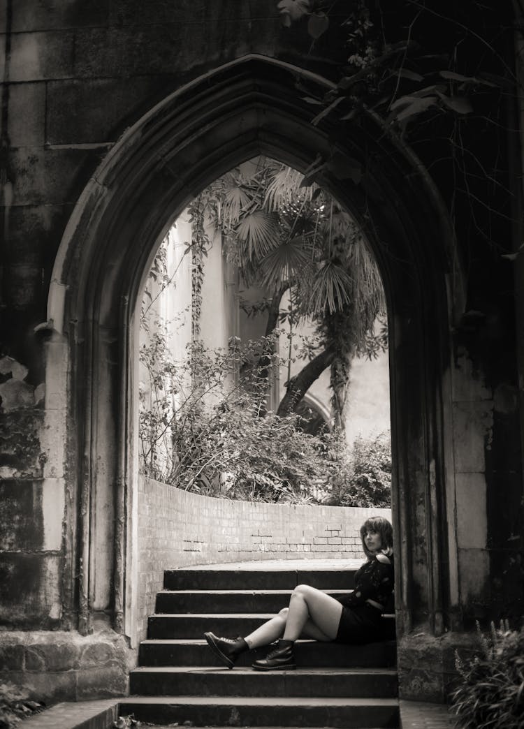 Woman In Blouse And Shorts Sitting In Archway Of Dunstan In The East Church, London