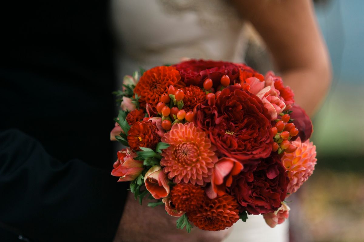Bride holding an autumn wedding bouquet with red and coral dahlias, garden roses, and orange berries