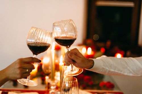Free Close-up of a couple toasting with red wine glasses in a romantic candlelit setting. Stock Photo