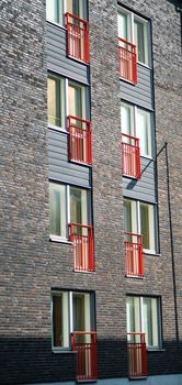 Vertical shot of a modern urban building facade with red balconies and brick walls.