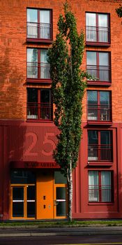 Vertical shot of a modern red brick residential building with unique facade and large tree.