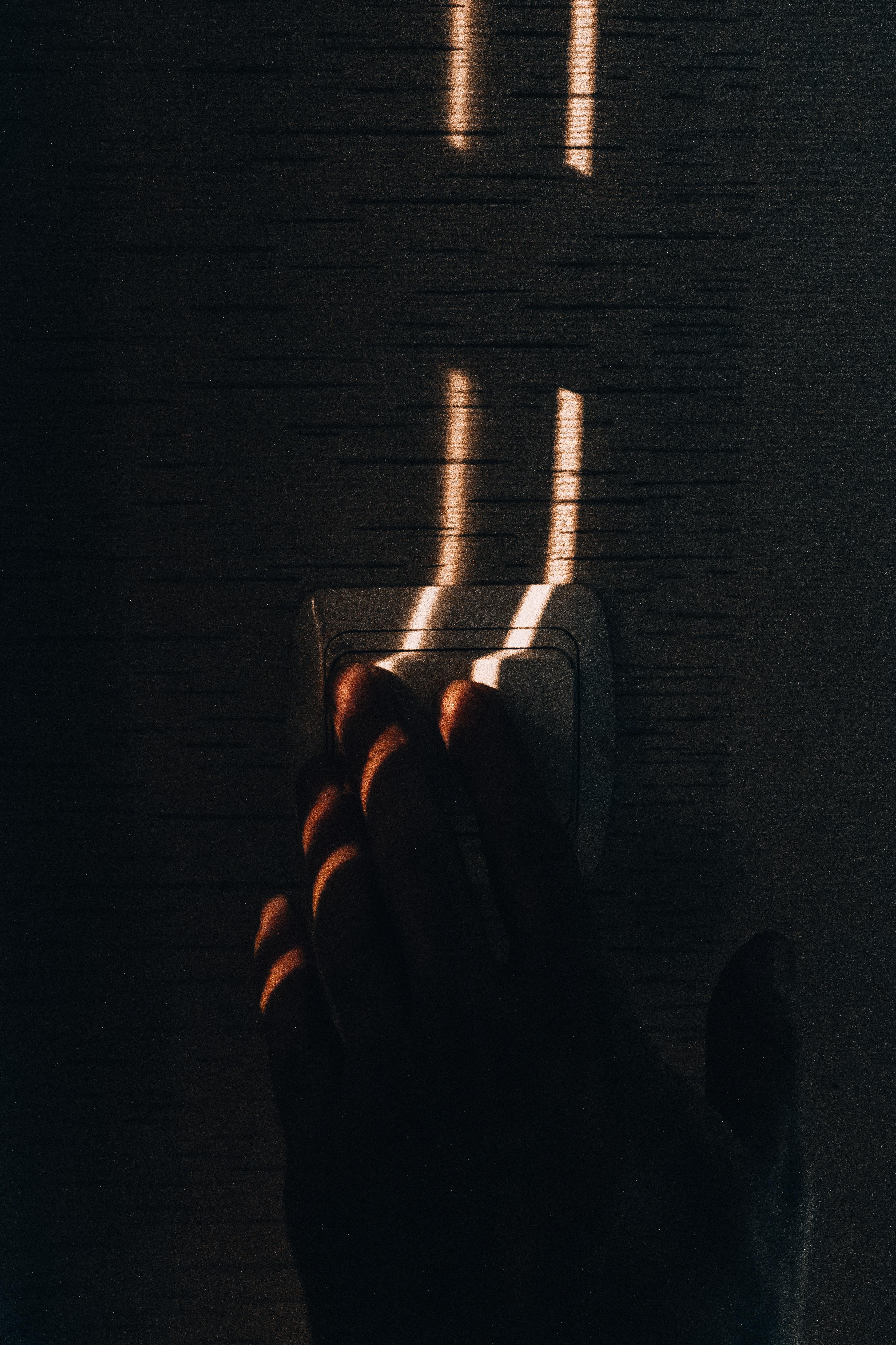 A hand reaching for a light switch, illuminated by dramatic sunlight, creating an artistic shadow effect.
