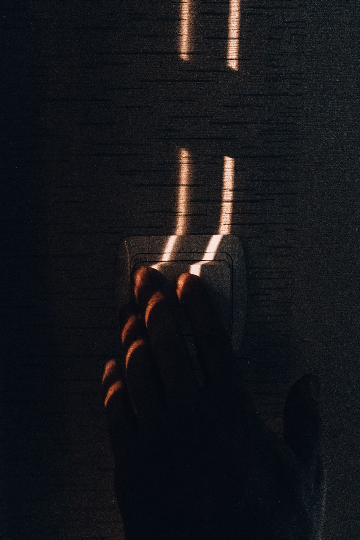 A hand reaching to touch a wall light switch in warm, directional light