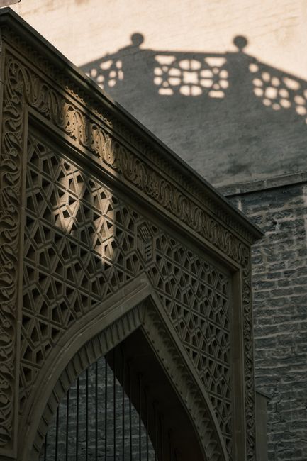 Intricately designed historical gate with striking shadow patterns on an old wall.