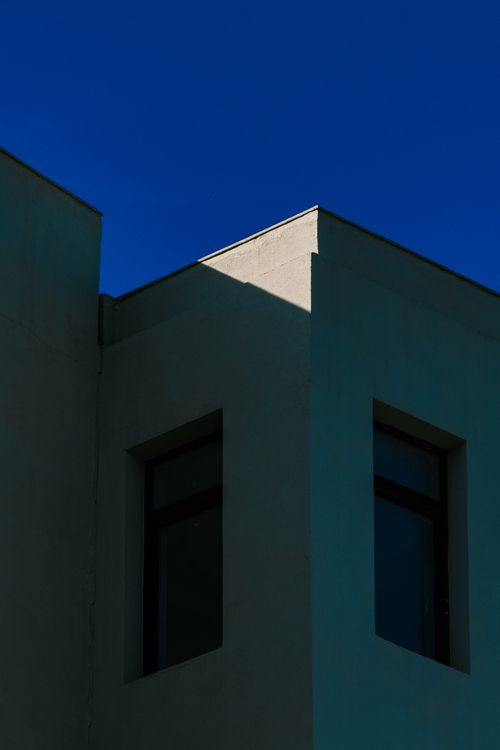 Free Corner of a minimalist building with deep shadows and clear blue sky, highlighting modern architecture. Stock Photo