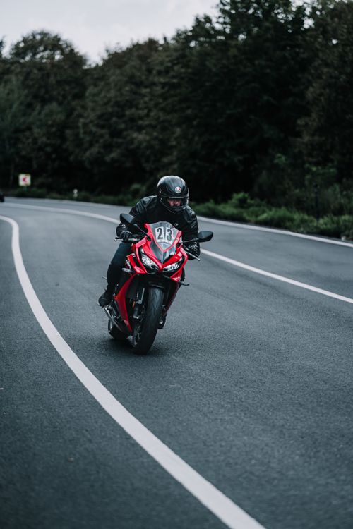Free A motorcyclist in gear riding on a scenic curved road surrounded by trees. Stock Photo