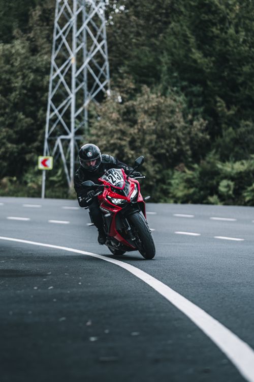 Free A motorcyclist rides a red sport bike on a curvy forest road, capturing a thrilling adventure. Stock Photo