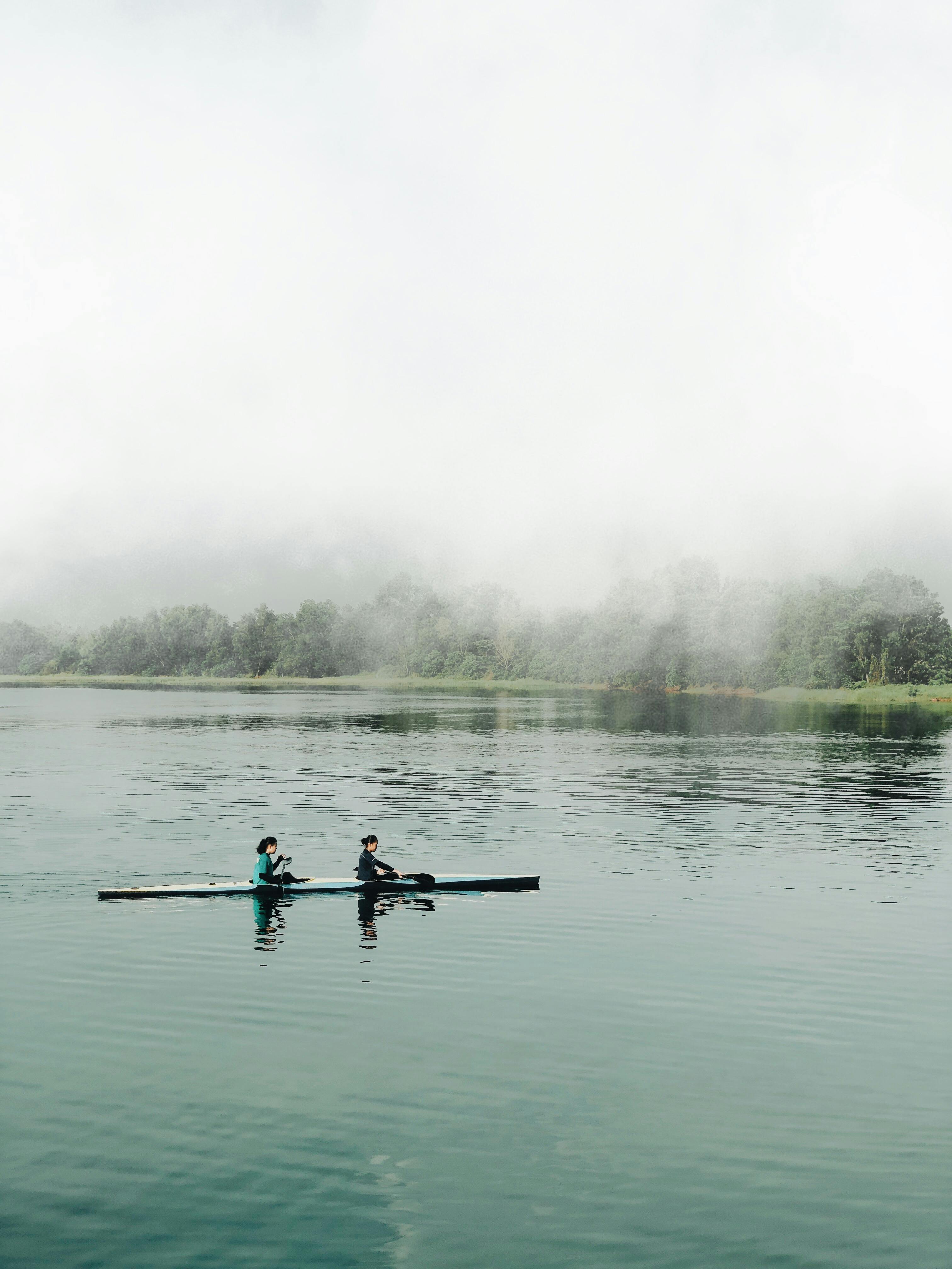 Two people kayaking on a tranquil lake shrouded in mist, creating a peaceful atmosphere.