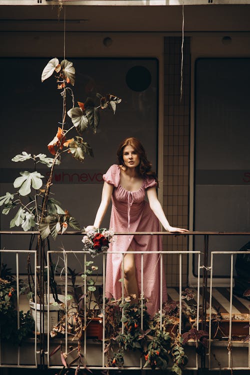 A woman in a pink dress standing on a balcony