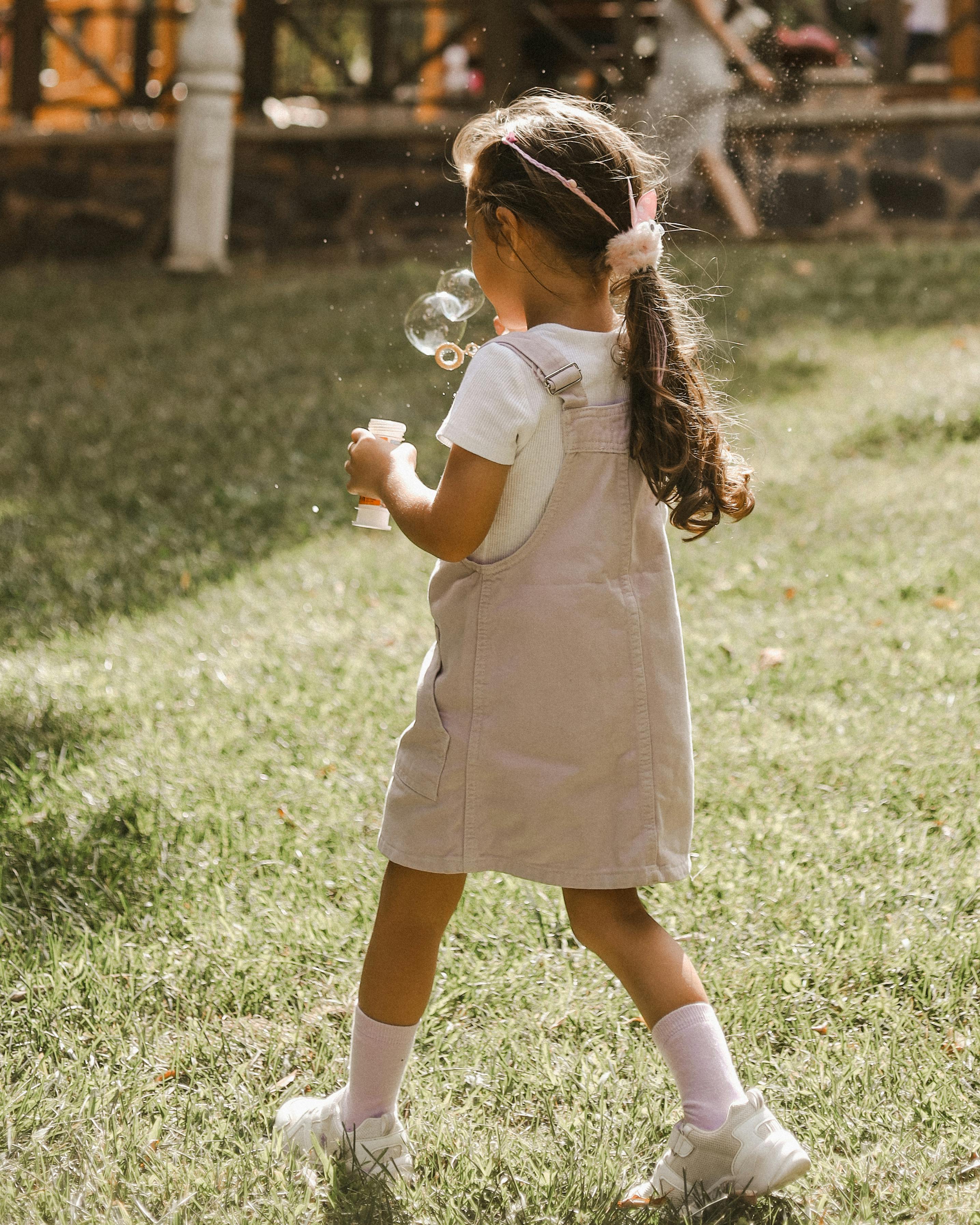 A girl in a pink dress joyfully plays with bubbles in a sunlit park.