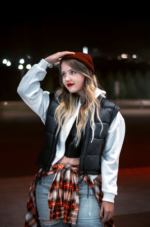 Free A fashionable young woman poses outdoors at night, wearing casual clothes and a red beanie. Stock Photo
