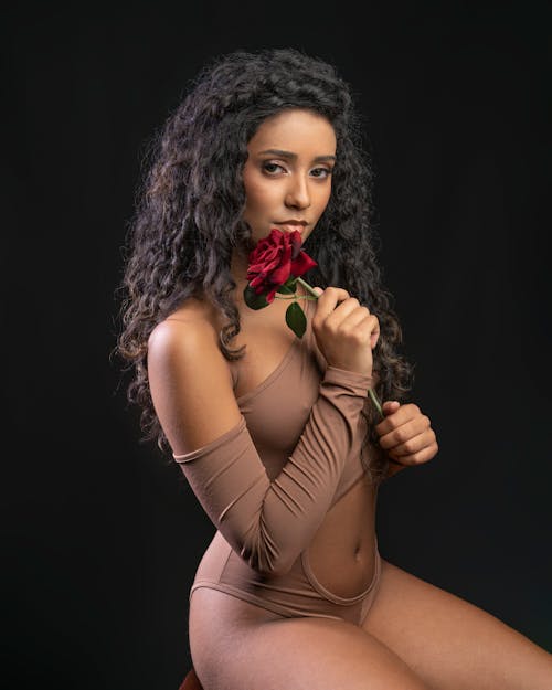 Studio Shot of a Young Woman in a Brown Bodysuit Holding a Red Rose 