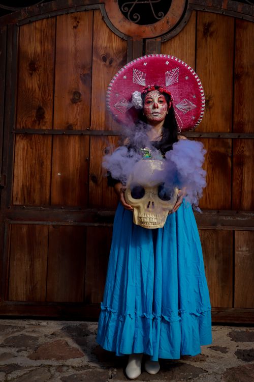 Free Catrina in vibrant Mexican dress holding a smoky skull for Day of the Dead celebration. Stock Photo