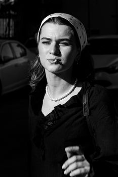 Stylish black and white portrait of a woman smoking outdoors, capturing bright sunlight and reflection.